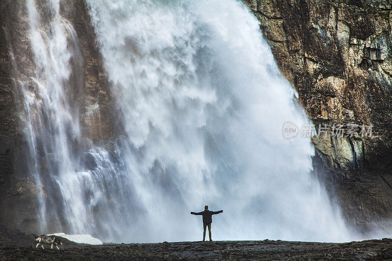 一个年轻人伸出双臂站在湍急的大瀑布下