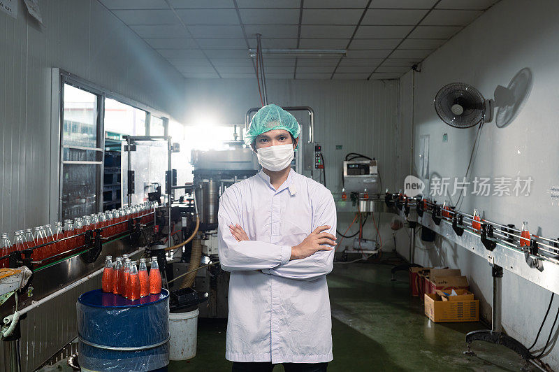 穿着无菌服的亚洲主管站在饮料加工厂的瓶装生产线旁