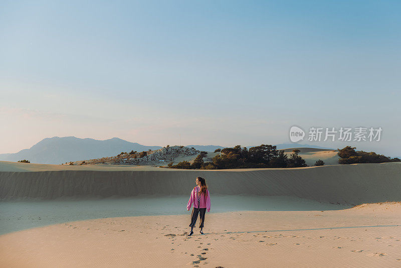 在土耳其海边的沙丘上，背着背包的女人凝视着风景优美的日落