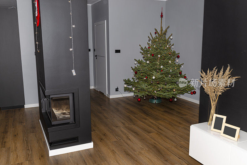 一棵装饰着小玩意的云杉圣诞树矗立在一座现代住宅的大厅里，客厅里有可见的壁炉。