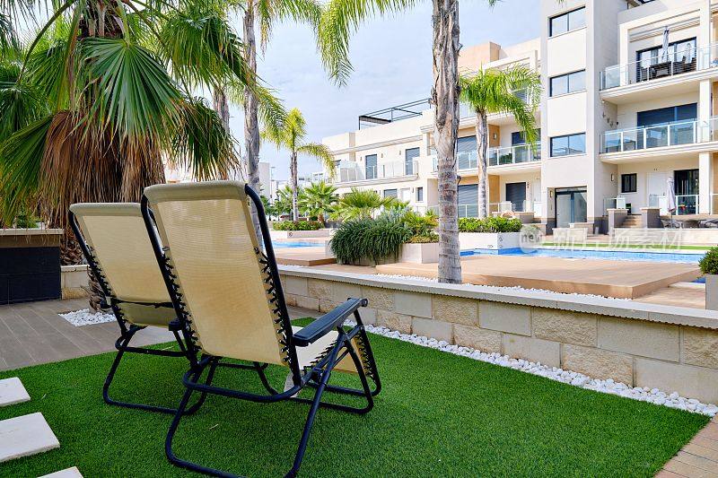 人造草坪上的两张躺椅俯瞰着现代化的公寓和游泳池