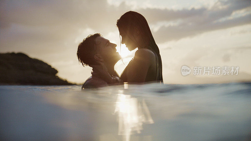 浪漫的异性情侣在金色的夕阳下在海里游泳。玩耍和拥抱