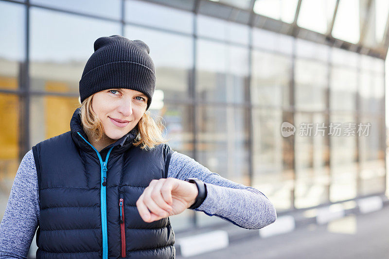 健身女子看着智能手表，计算燃烧的卡路里。女子在锻炼后放松地站着，用智能手表检查心率。快乐的跑步者在户外运动后检查智能手表