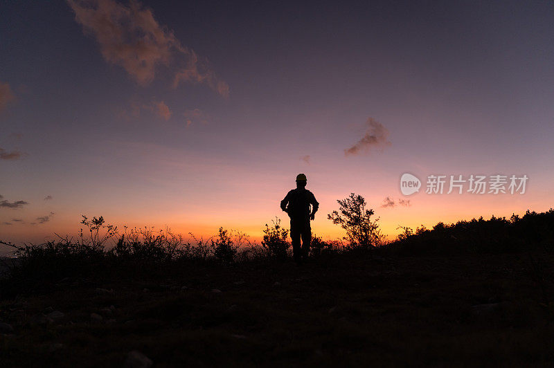 黄昏时一个人走在山顶上的剪影，面对着红色的天空和夕阳