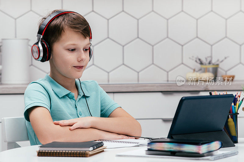 青春期前专注的男孩的肖像，坐在笔记本电脑旁，看着平板电脑的屏幕，在家里进行在线课程。