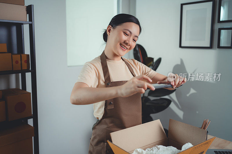 亚洲女卖家在打包货物准备发货前用智能手机拍照。