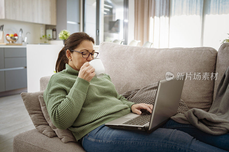 女人躺在沙发上用笔记本电脑喝咖啡