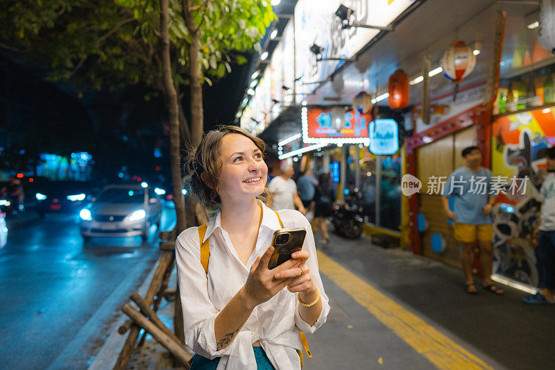 一个拿着智能手机的女人晚上走在城市里