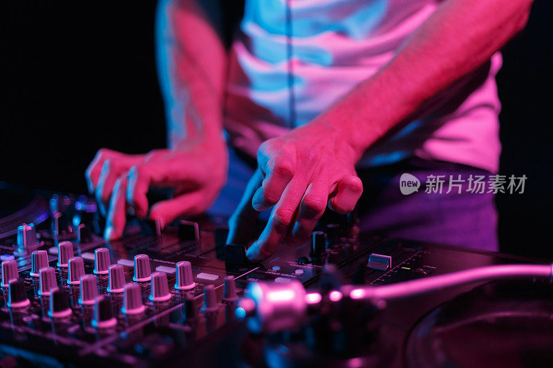 DJ在夜总会的派对上播放音乐。近距离照片的专业唱片播音员混合黑胶唱片与混音器设备
