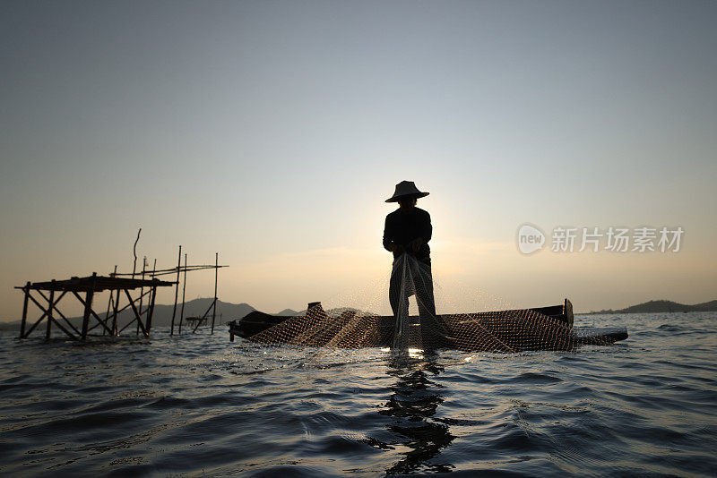 渔民在船上撒网捕鱼的生活方式，剪影渔民撒网从水库捕鱼