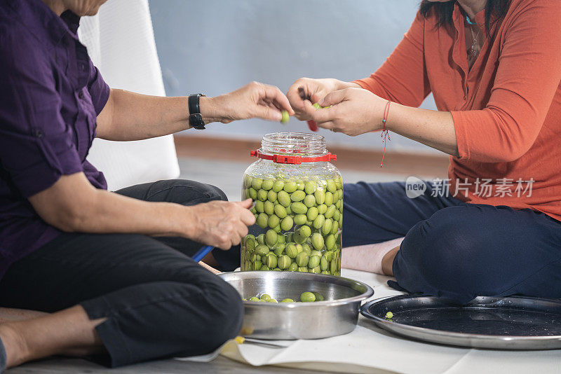 老年妇女和成熟的成年朋友准备绿橄榄调味料的照片