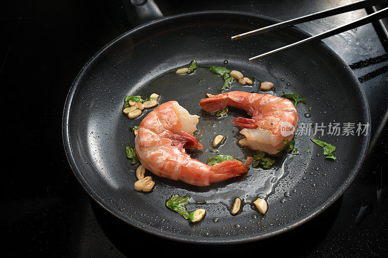 两只大虾在黑色煎锅里用橄榄油与大蒜和香草一起煎炸，准备一顿美味的海鲜大餐，配上新鲜的甲壳类动物，复制空间，精选焦点