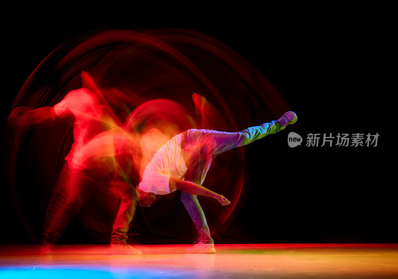 年轻活泼的家伙跳舞嘻哈，霹雳舞对黑色工作室背景在红色霓虹灯与运动模糊。