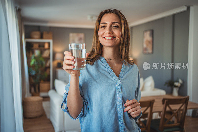 一个微笑的年轻美女的画像，手里拿着一杯新鲜干净的饮用水。健康生活方式和液体摄入的概念