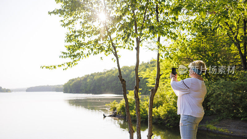 可持续发展的旅游。一名女子在宾夕法尼亚州贝尔茨维尔州立公园阳光明媚的湖边捕捉大自然