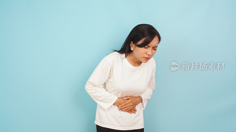 一名亚洲女性疼痛地捂着肚子，可能是痛经，浅蓝色背景