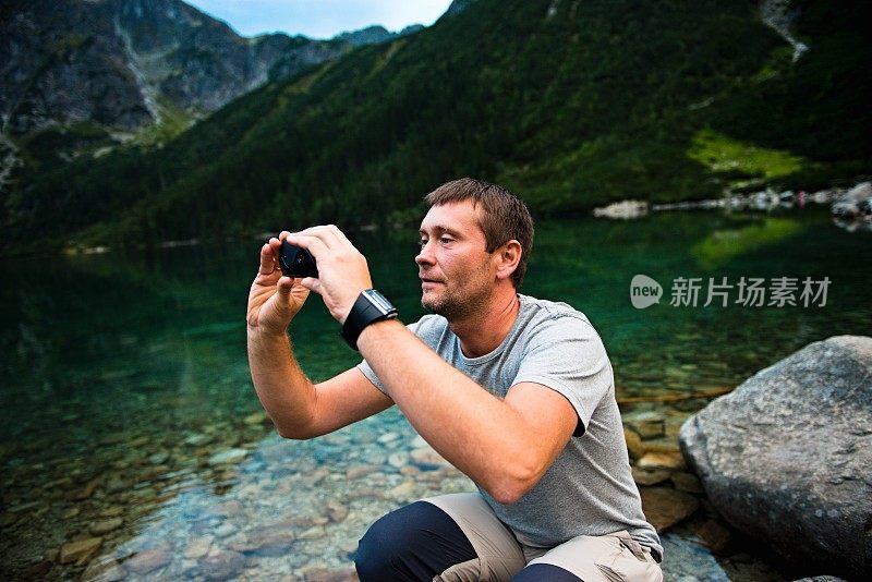 一名成年男子，在太特拉喀尔巴阡山脉的摩尔斯基奥科湖用智能手机拍照，