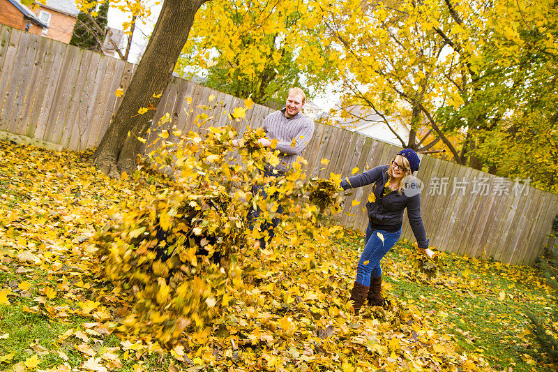 一对年轻夫妇在院子里耙树叶时玩耍