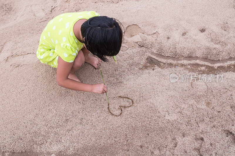 亚洲女孩在沙子上画心