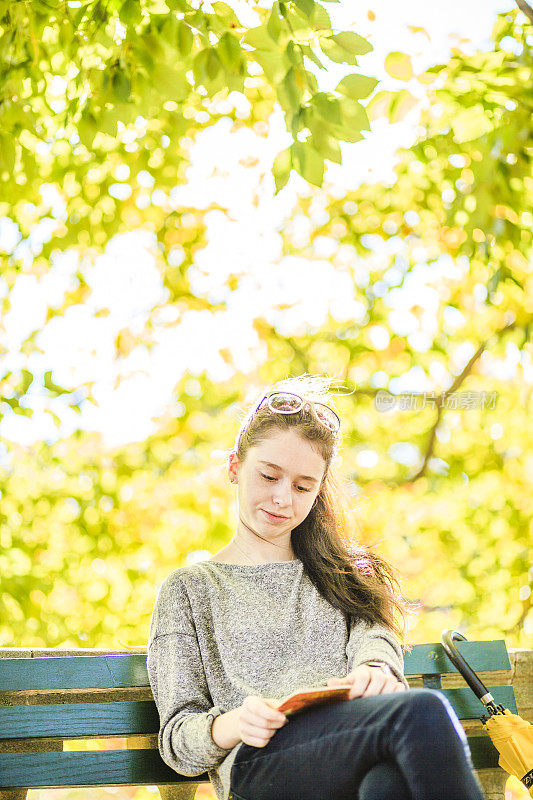 一个十几岁的女孩在秋天的公园里看书