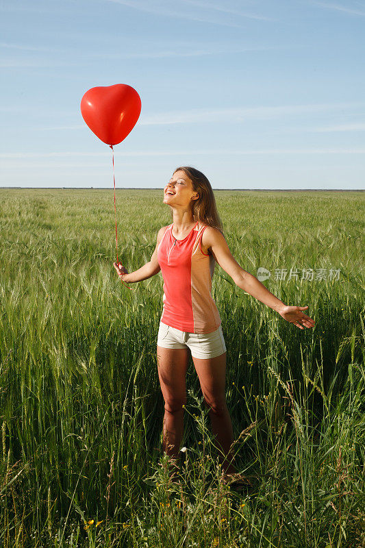 拿着红色气球的女孩站在操场上