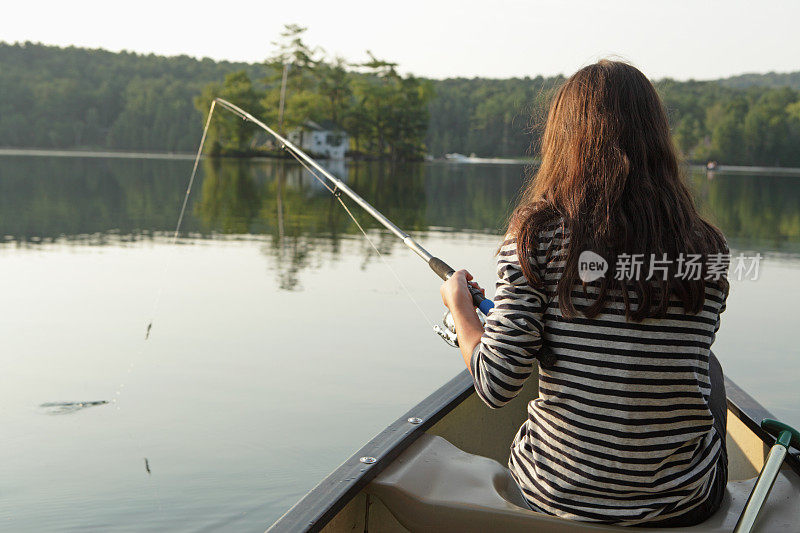 年轻的女孩在平静的湖面上乘着独木舟钓鱼