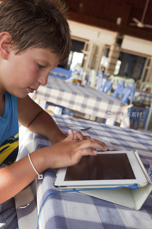 一个男孩坐在咖啡馆里用着平板电脑。
