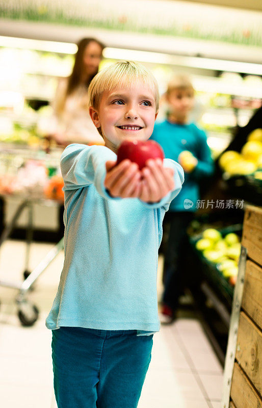迷人的金发小女孩在超市吃着红苹果