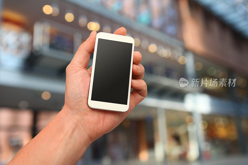 手持智能手机，可定制的空白显示，散焦购物中心背景
