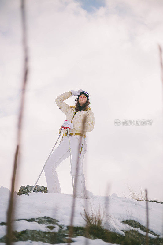 近景美丽的年轻女子在冬天的衣服站在一边，手拿木棍的背景雪山