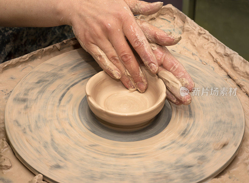 在陶轮上制作陶碗的过程中，妇女手拿陶土