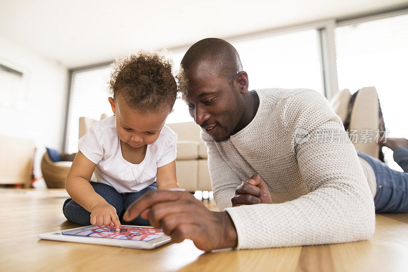 非裔美国父亲带着家里有平板电脑的小女儿。