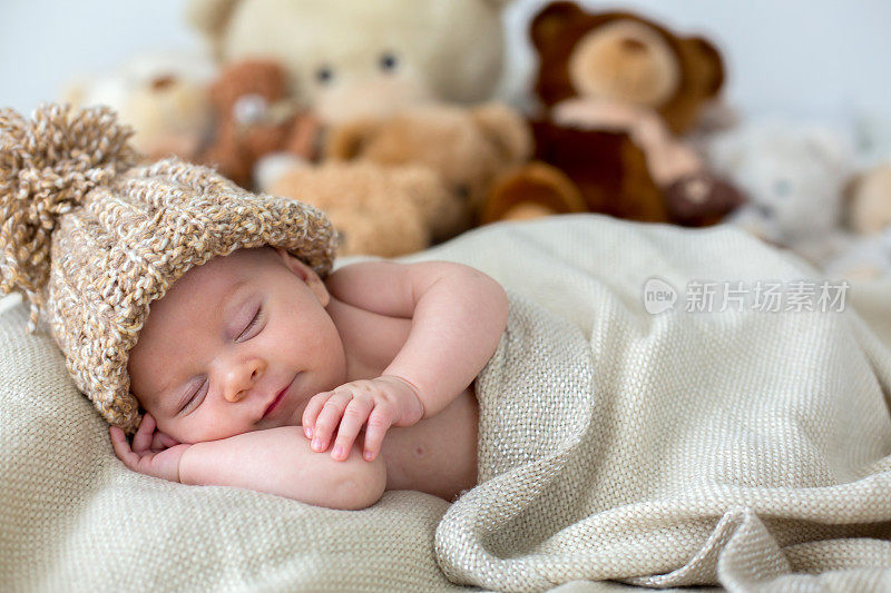 刚出生的小男孩，和泰迪熊一起睡在家里的床上