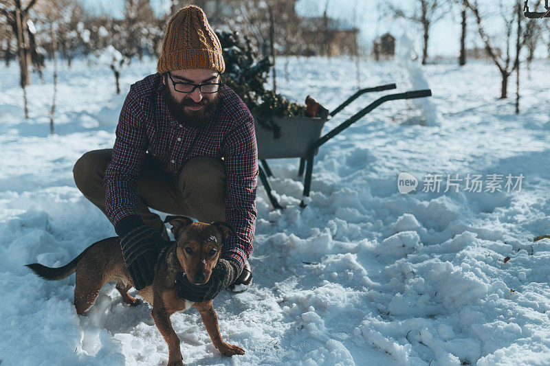 一个英俊的男人在一个下雪的冬日抚摸着一只狗