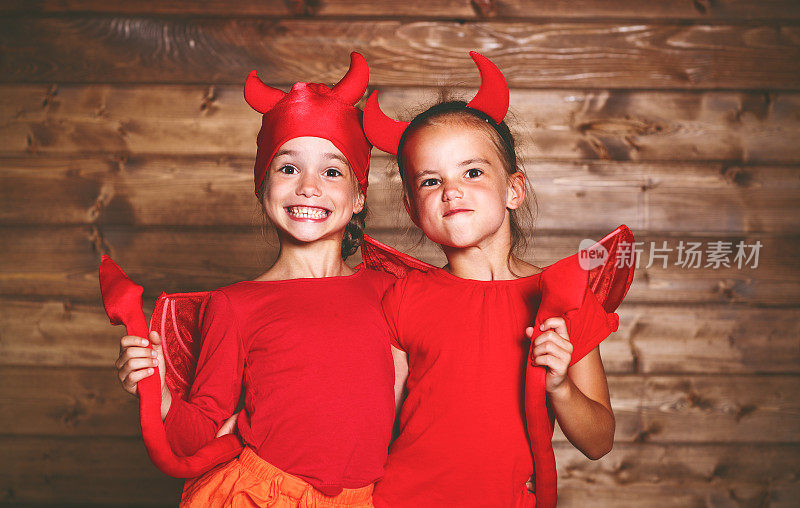 节日万圣节。滑稽滑稽的姐妹双胞胎孩子在狂欢节的服装上魔鬼在木制