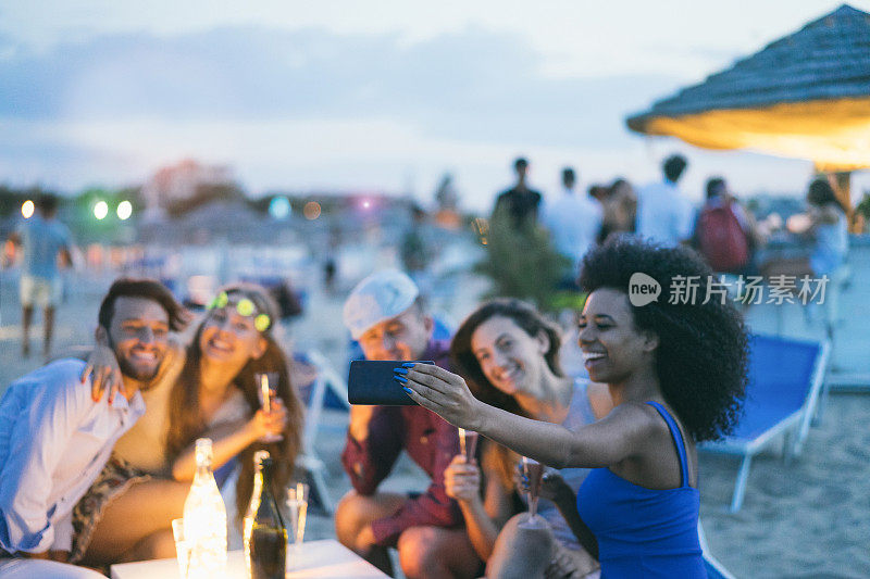 快乐的朋友与智能手机自拍在海滩派对户外-年轻人有乐趣在kiosk酒吧喝香槟-关注非洲女孩手机-青春和夏天的概念