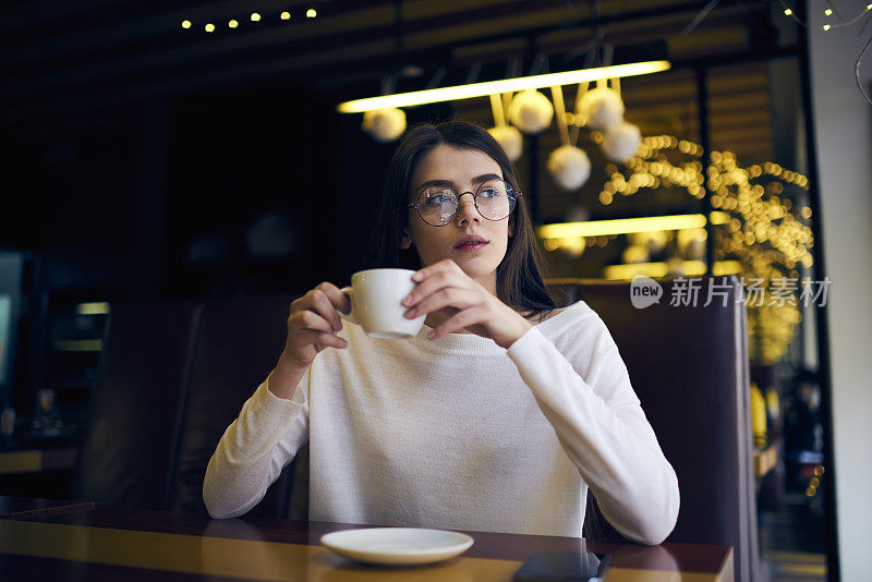 年轻迷人的时髦女孩戴着眼镜享受芳香咖啡思考一天的计划，而坐在咖啡馆，迷人的女性开始的一天与美式早餐集中的想法