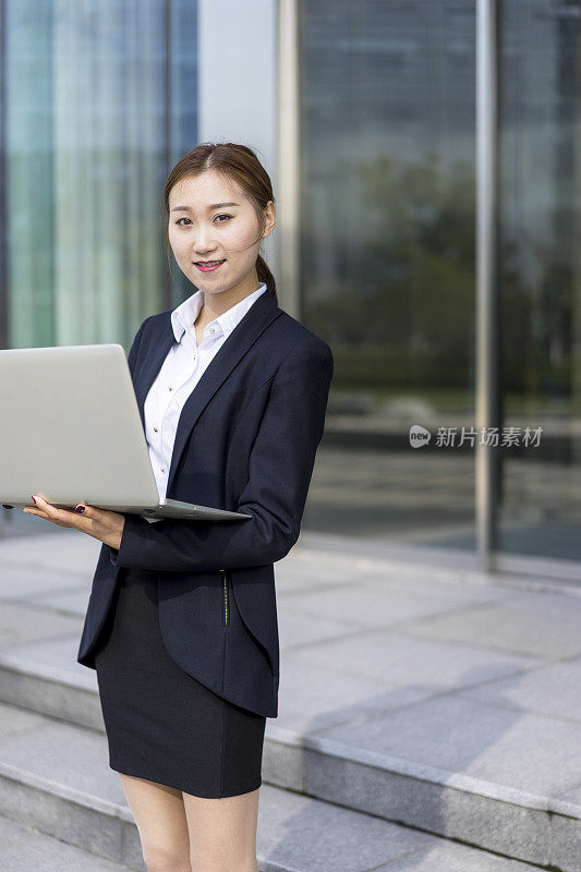 穿着正装的年轻女子在办公大楼外使用笔记本电脑