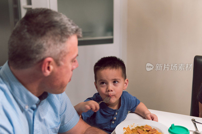一个小男孩在吃饭的时候抬头看着他的父亲