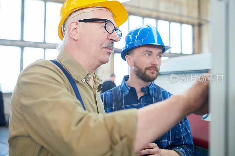 在工厂选择机器程序时，安全帽上的工作人员在控制面板上按按钮