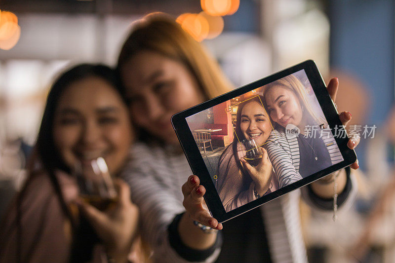 近距离快乐的亚洲朋友在一个酒吧里玩，而与数字平板电脑自拍。