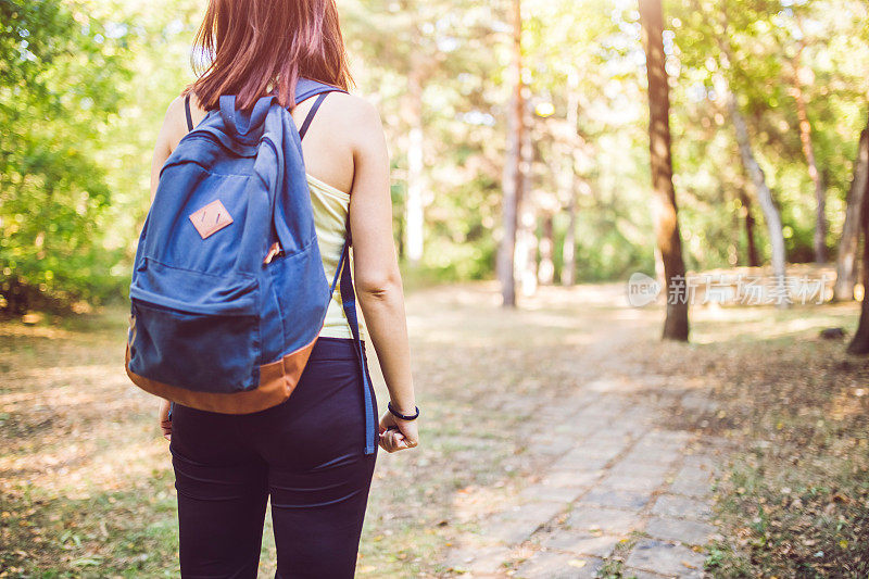 女旅行者背着背包走在森林里的小路上。