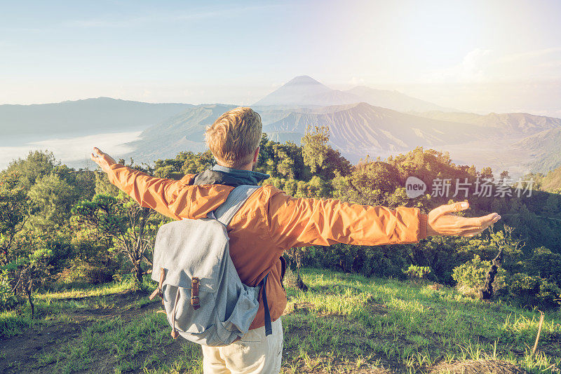 在印度尼西亚，年轻人徒步旅行，手臂伸开站在火山的山顶上，人们旅行的乐趣，冒险的概念，成功和成就