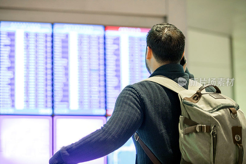 一名男性旅客在机场候机楼阅读到达和出发牌