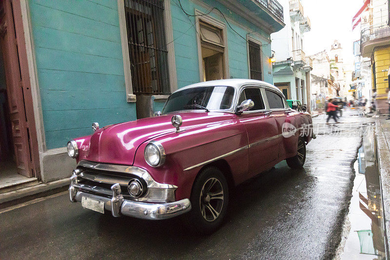 一辆粉色复古车行驶在古巴的街道上