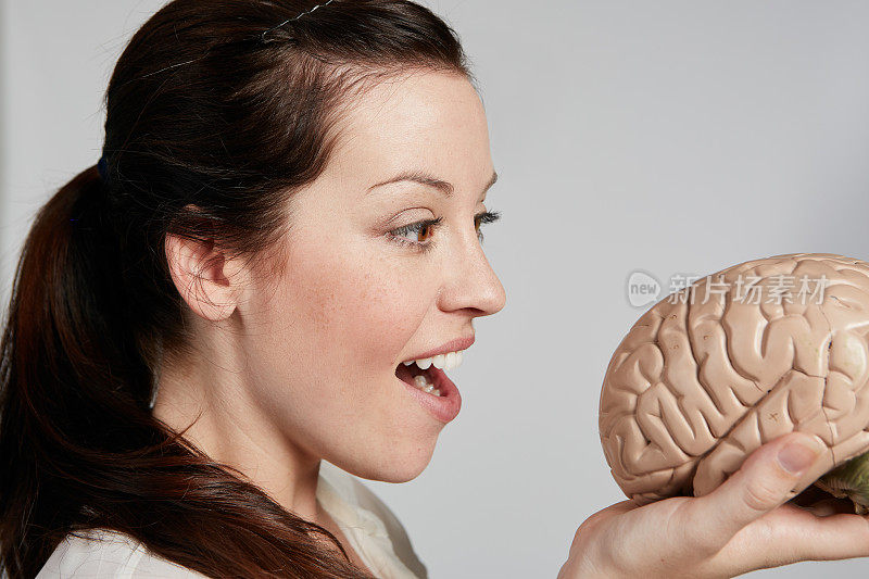 漂亮的棕发女人张开嘴看人类大脑的解剖模型
