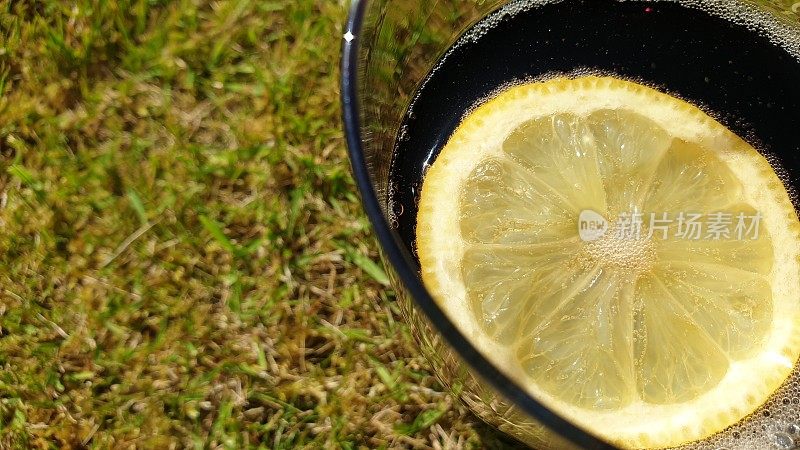 在草的背景下，一杯可乐里的一片柠檬