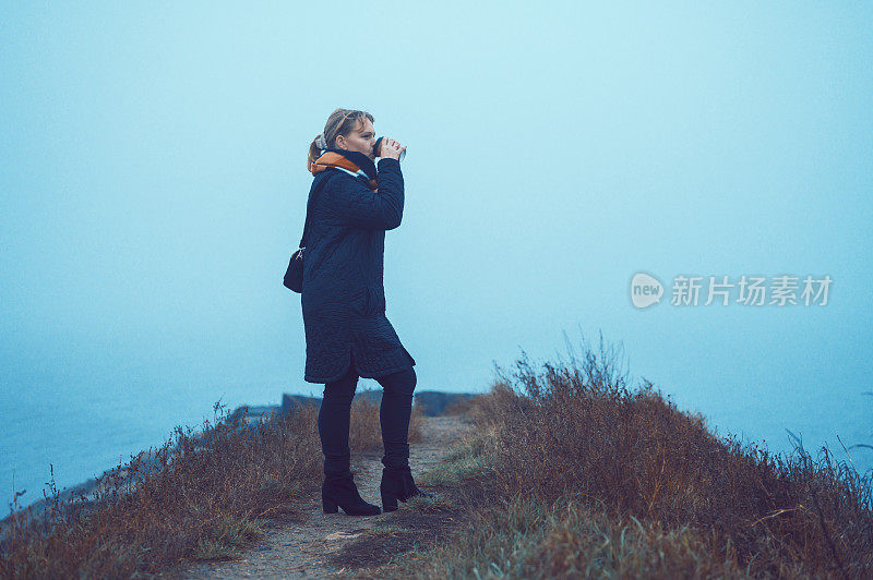 女人喝一杯热咖啡或茶，因为她站在外面在寒冷的天气