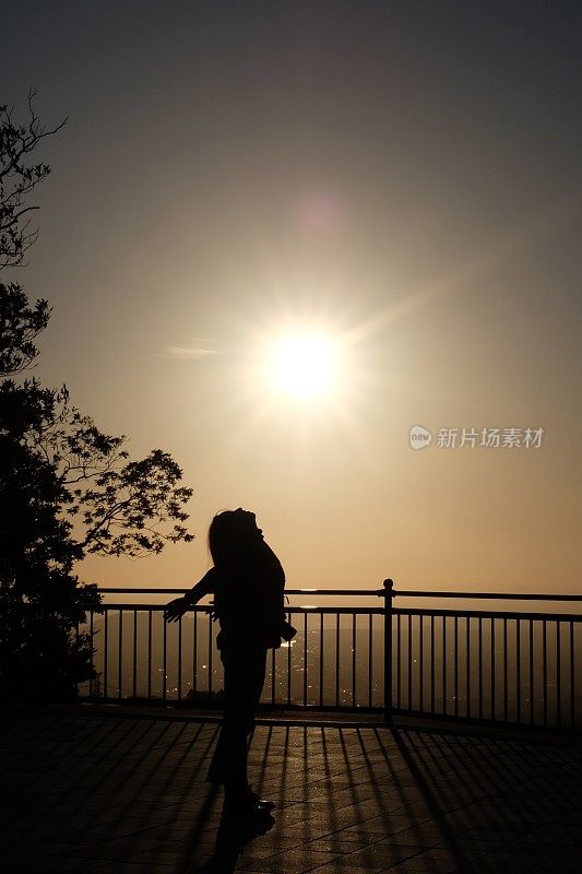 日落时分，一位年轻女子在观景台上伸懒腰