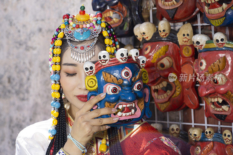 2019年6月23日，中国西藏拉萨城关区，一名年轻美丽的化妆女孩身穿藏族传统服饰和珠宝，他正在试戴藏族传统面具